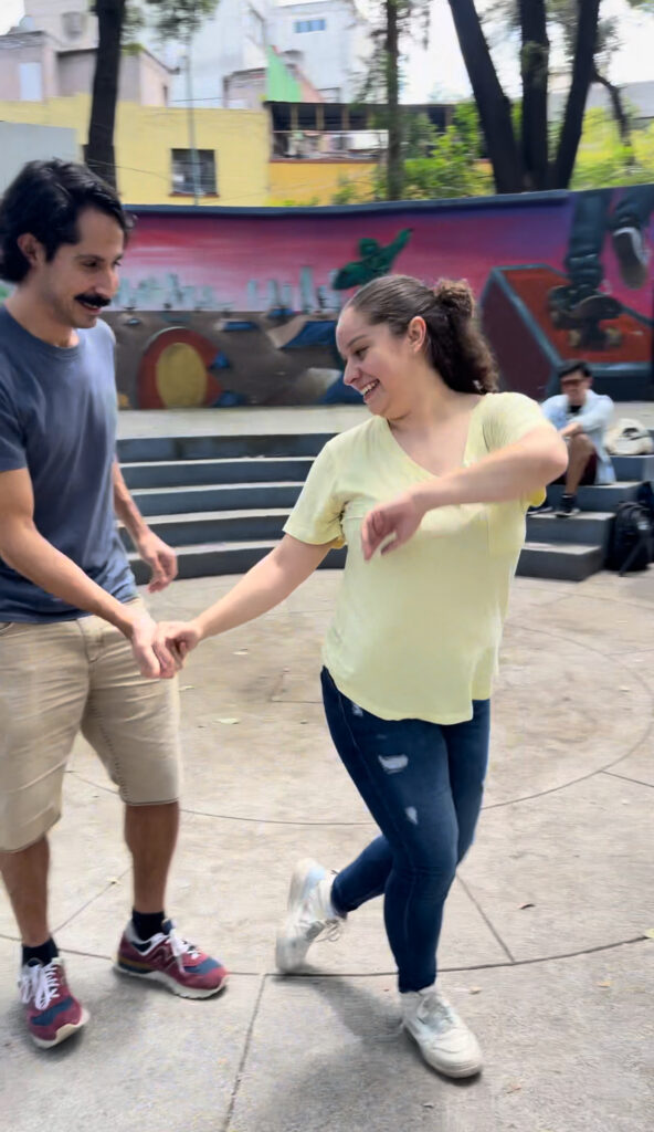 Two dancers performing West Coast Swing in a vibrant plaza in Mexico City CDMX Ciudad de México, showcasing smooth moves and joyful expressions.