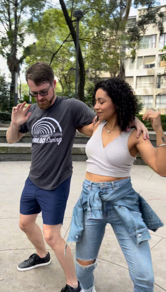 A couple dancing West Coast Swing in an open plaza in Mexico City CDMX Ciudad de México, surrounded by historic architecture and lively energy.